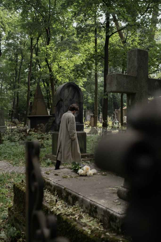 a man in a trench coat walking at a cemetery