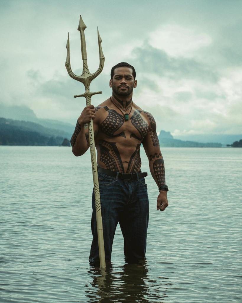man in the aquaman costume standing in the water with a trident